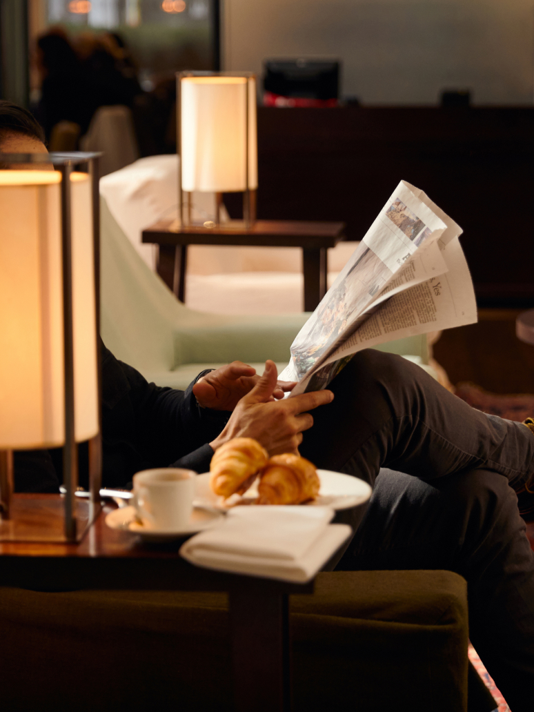 Man reading newspaper at The Mercer with a coffee and croissant