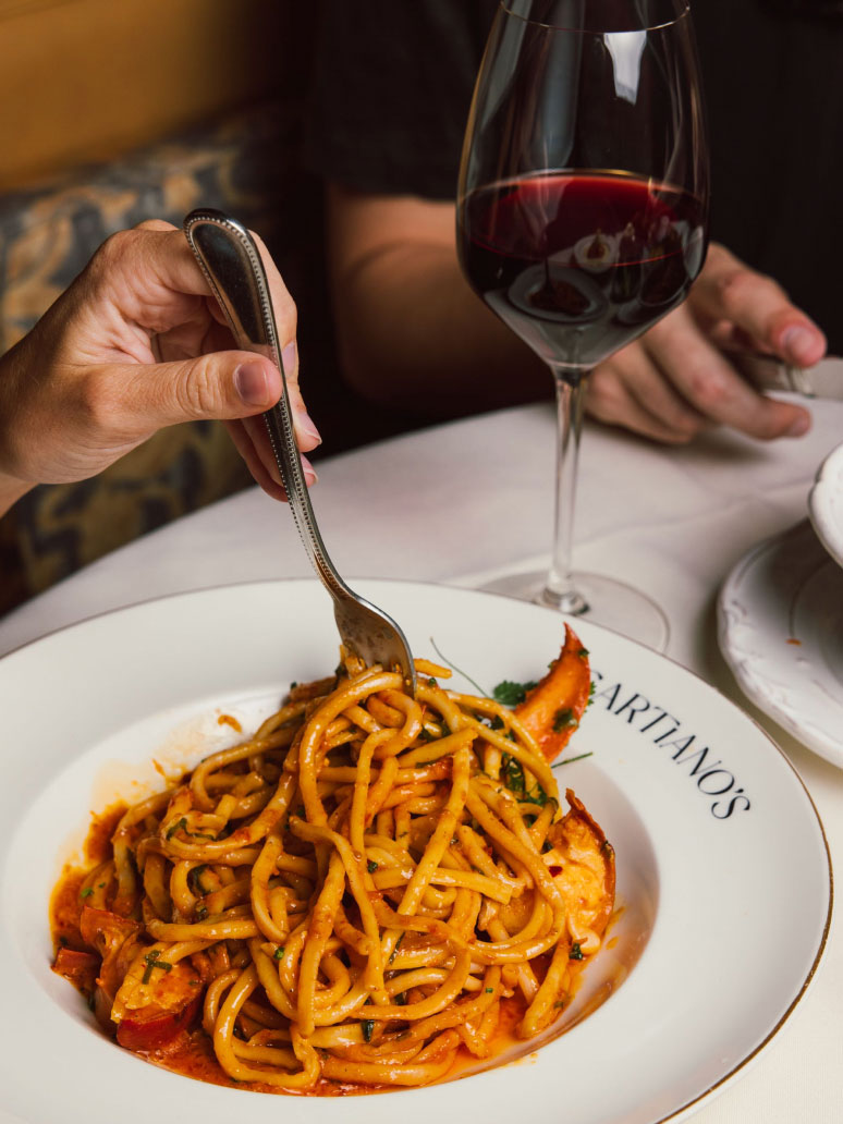 A closeup of a pasta dish and glass of wine at Sartianos