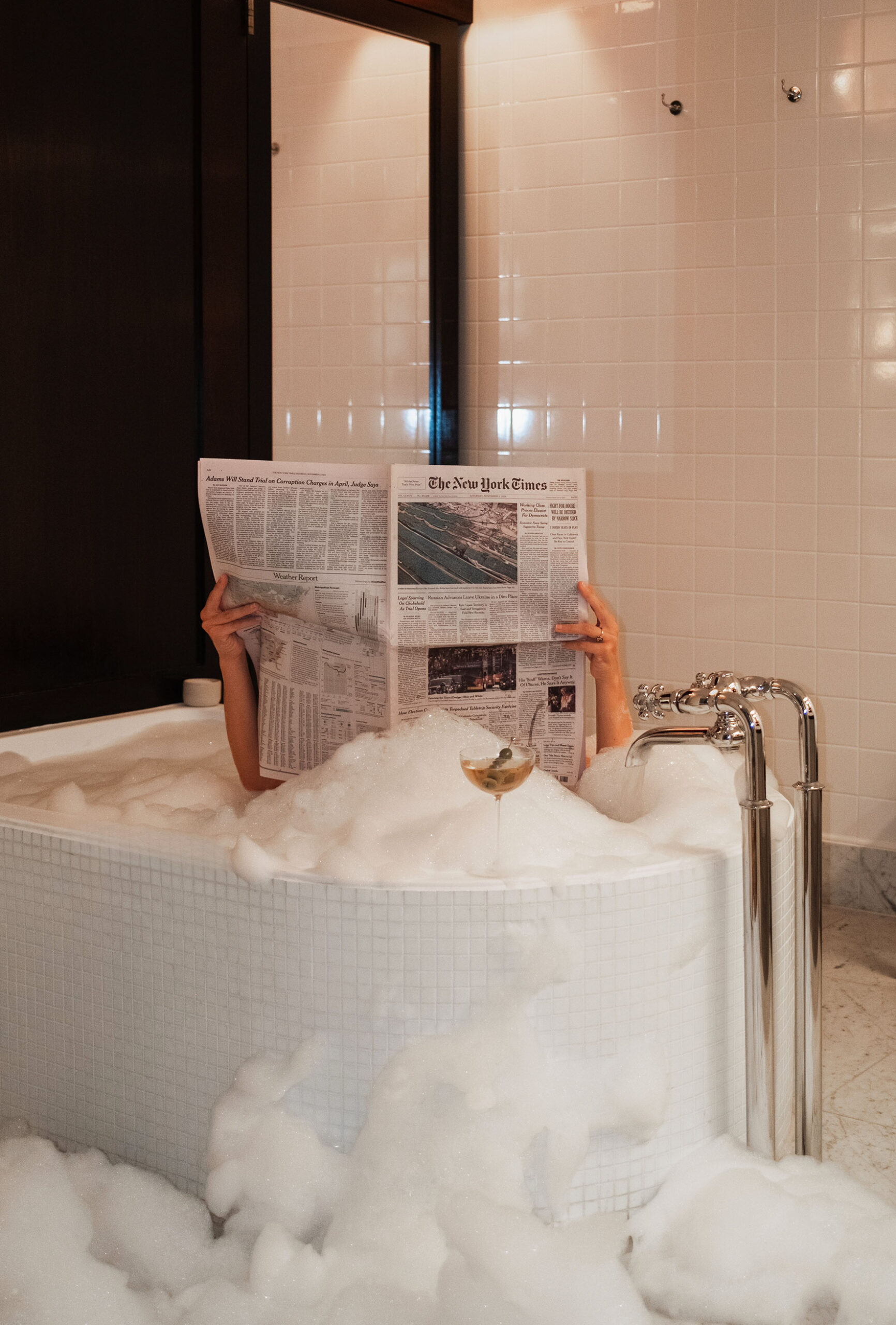 A hotel guest reading their complimentary news paper in a bubble bath